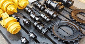 construction A selection of new replacement parts for the chassis of heavy equipment machinery lies on a black wooden pallet.