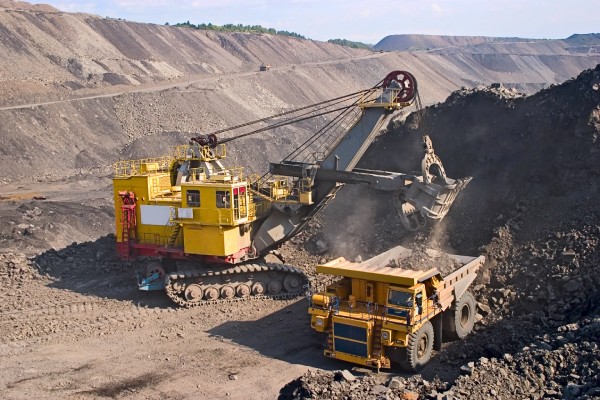 Two big yellow mining trucks sit in the middle of a big mining facility, moving large amounts of material.