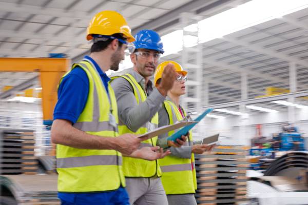 A supervisor and workers having a discussion in a warehouse, surrounded by shelves stacked with boxes and various goods.