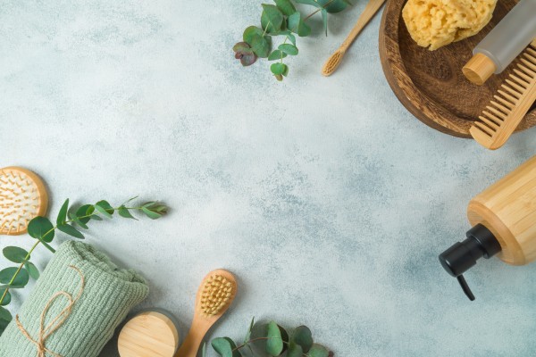 A collection of eucalyptus sprigs and wooden hair care supplies. They lay on a blue backdrop with leaves sitting around them.