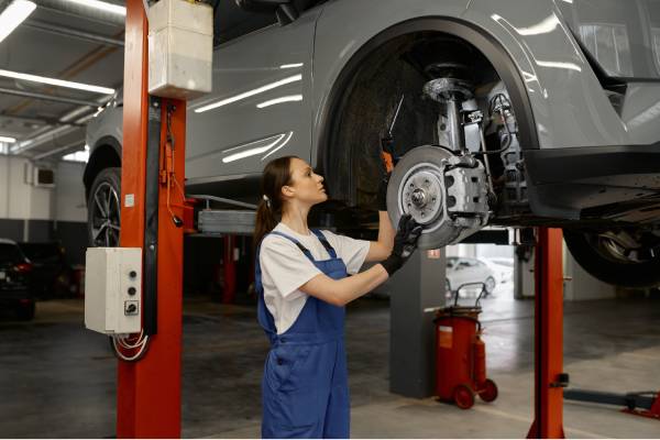 A female mechanic inspecting the brake system of a vehicle. The car is currently hoisted up in the air.