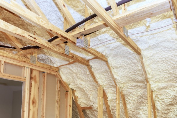 A building with bare studs and wiring. The walls and ceiling have been filled with white spray foam insulation.