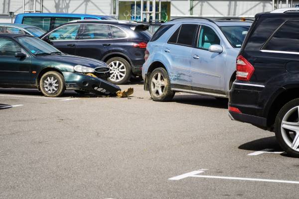 Two cars in a parking lot in a car accident. One car lost its bumper while the other was pulling out into the aisle.