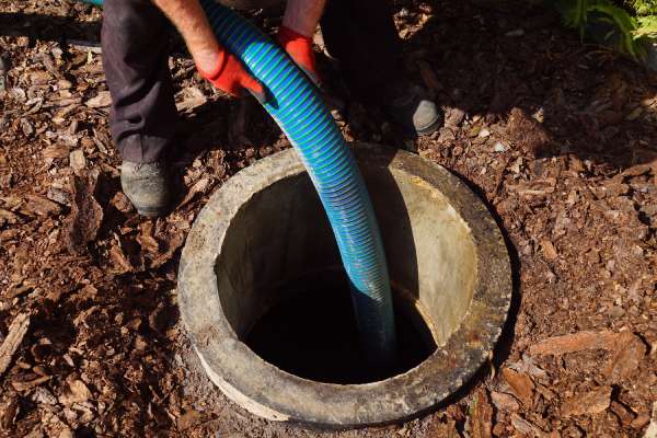 A person holding a pump and putting it inside a septic tank. There are rocks and dirt around the tank.