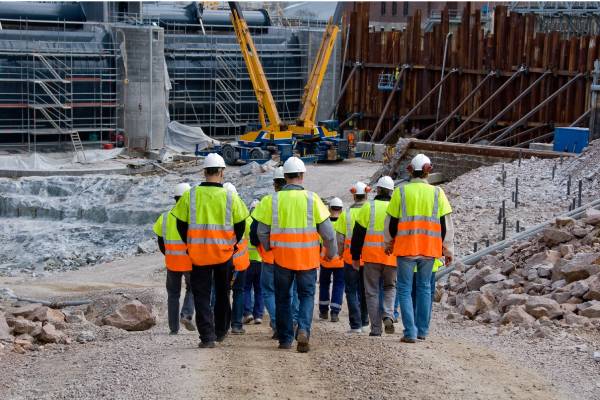A group of construction workers walking away, wearing bright orange and yellow safety vests and hard hats.