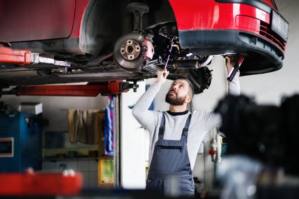 An automotive mechanic working on a vehicle from the underside. The car is sitting on a mechanical automotive lift.