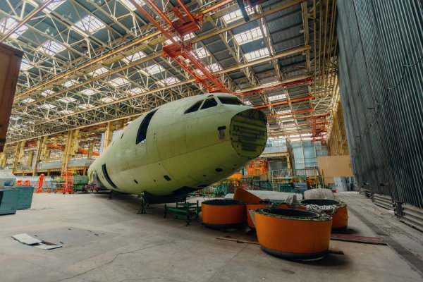 The metal frame of a plane's cockpit and fuselage sits in large warehouse awaiting assembly completion.