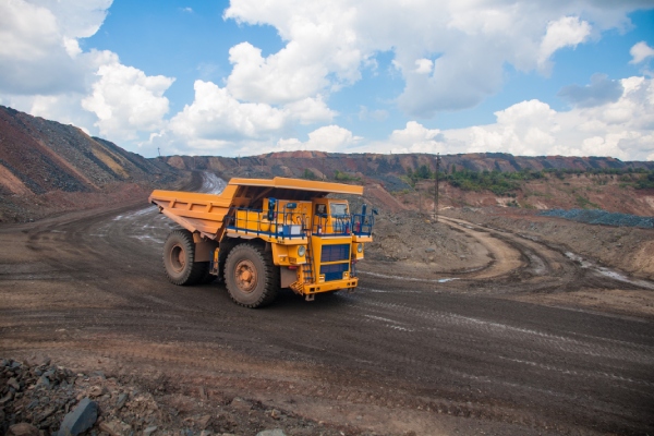 A large, yellow mining dump truck drives around a mining quarry with a load of ore and other minerals.