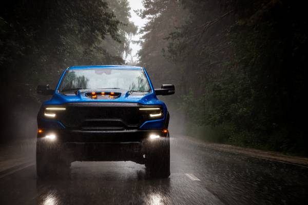 A blue pickup truck drives on a road through a forest and in the rain with no other cars on the road around it.