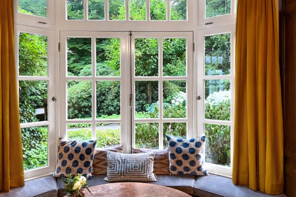 A bay window contains yellow curtains, leather cushions, tan pillows with blue polka dots and stripes, and a wooden table.
