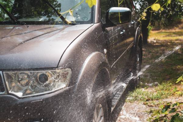 A gray SUV sits on a section of patchy grass as a stream of water hits the front driver's side wheel.