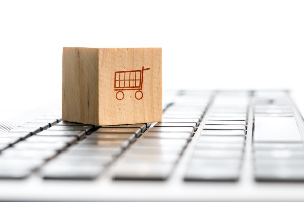A small wooden block has the outline of a red shopping cart on one side. The block sits on a laptop keyboard.