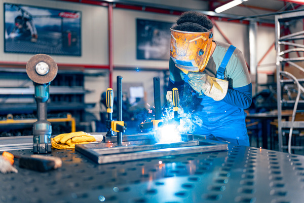 A person works in a metal shop welding metal together. The employee wears a yellow welding mask and gloves.