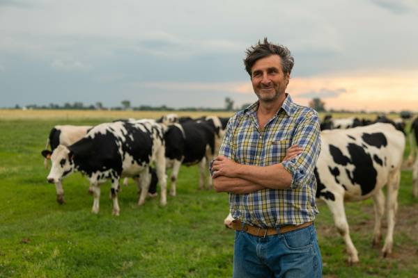 crop farmers livestock A smiling farmer standing with his arms crossed in a grassy field. Grazing cattle stand behind him under an overcast sky.
