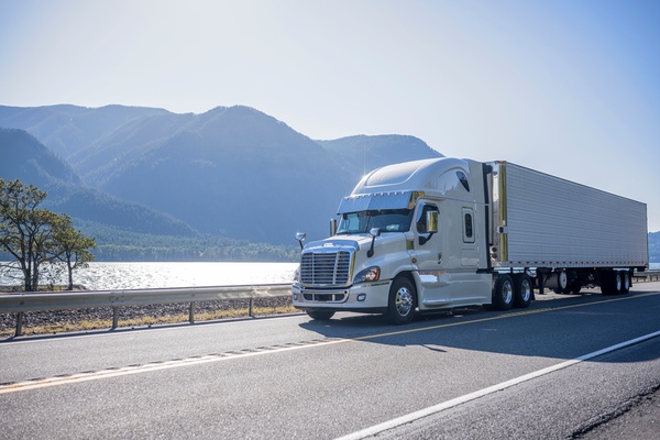 truck A white and chrome semi-truck riding down a highway with mountains in the background. It's a sunny day.