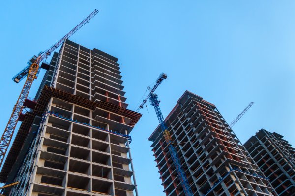 Three high-rise buildings with large cranes positioned next to each building on a sunny day with a blue sky.