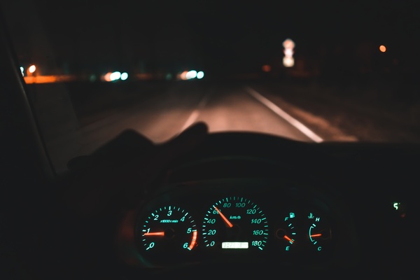 A motorist behind the wheel of their vehicle as they drive down an empty road at nighttime. The dash lights are on.