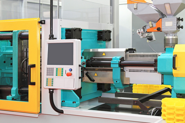 An injection molding machine features turquoise, yellow, and white components with a panel showing a blank screen.