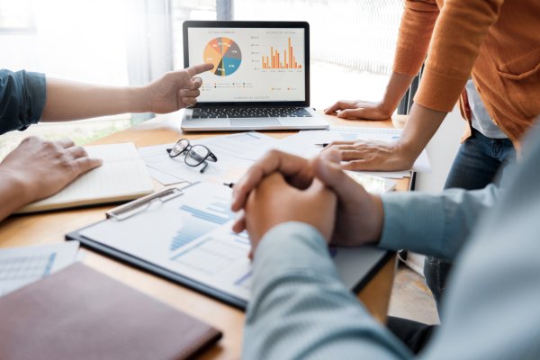 A close-up of a team of marketers pointing to and discussing the PowerPoint with a pie chart of results.