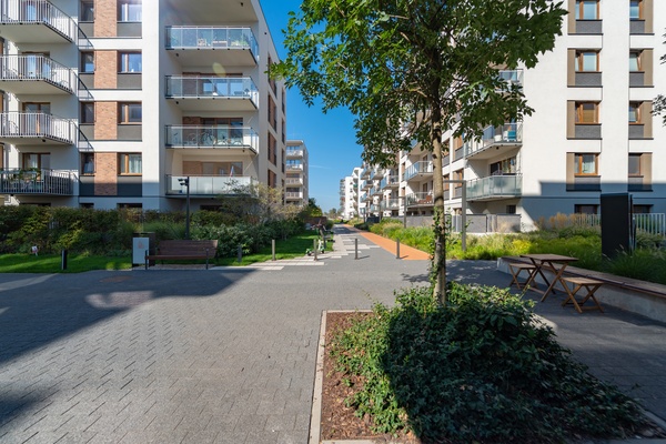 A pedestrian promenade in a residential housing area features seating near a table and lush greenery.