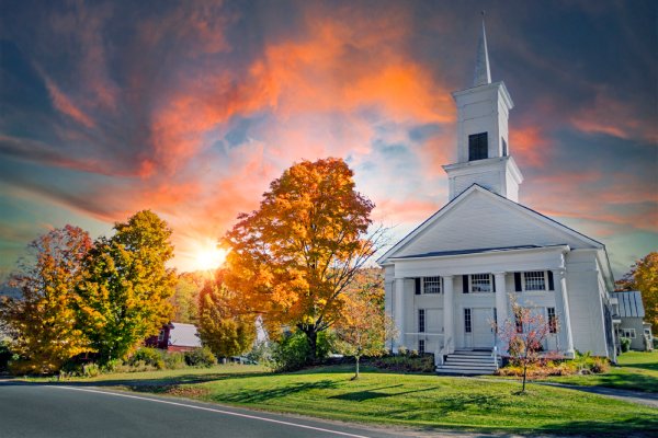A beautiful sunset with colorful clouds above a white church. The church lawn is lush and green with a few trees.