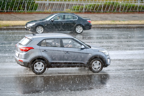 A black vehicle and a gray vehicle are driving on a wet road, passing each other in opposite directions. It's raining.