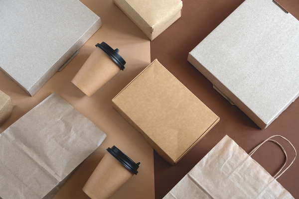 A top-view of flat disposable cardboard blank food packaging placed on a beige and brown background.