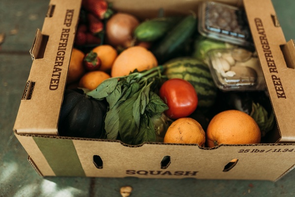 A cardboard box labeled "keep refrigerated" that holds oranges, tomatoes, strawberries, blueberries, onions, and more.