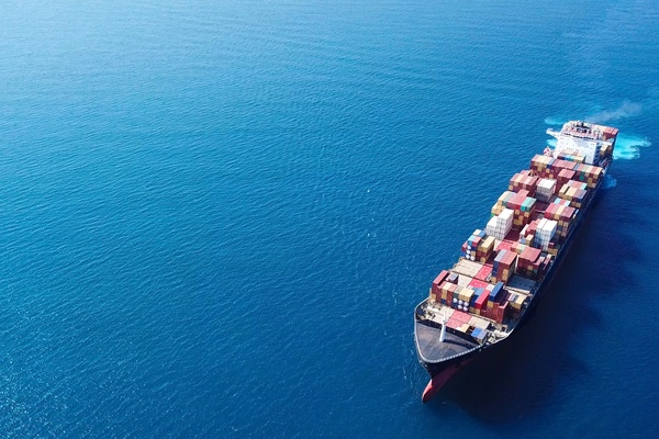 A large cargo ship stacked with shipping containers floats in the open ocean with no land visible in any direction.