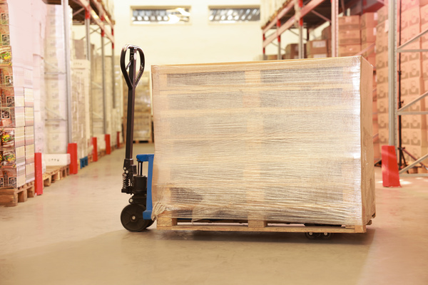 A stack of wooden pallets on a manual forklift with a stretch wrap film wrapping in the middle of an aisle in a warehouse.