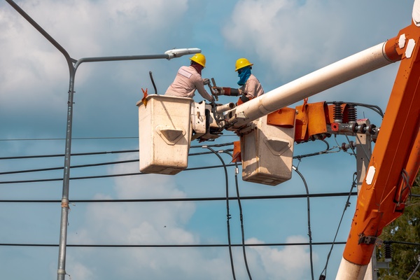 Two people on a boom lift are working on a power line with the utility pole. Also behind them is a street light.