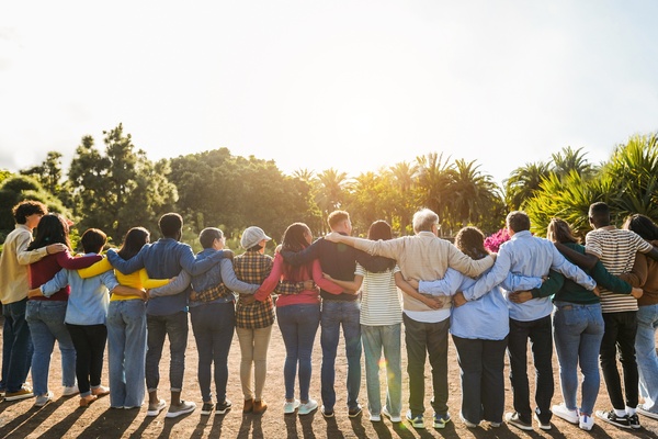 On a sunny day, a group of multigenerational people stands in a line with their arms wrapped around each other.