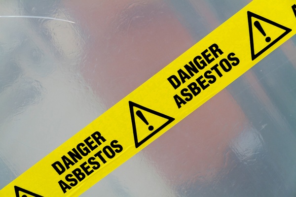 Yellow caution tape stretches diagonally across the frame. It says "DANGER ASBESTOS" with exclamation mark icons.