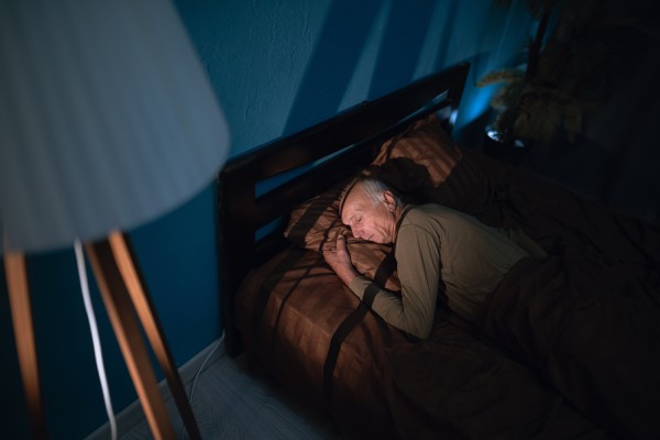 An overhead view of a man lying in a bed at night while sleeping on his side. An exterior light streams into the room.