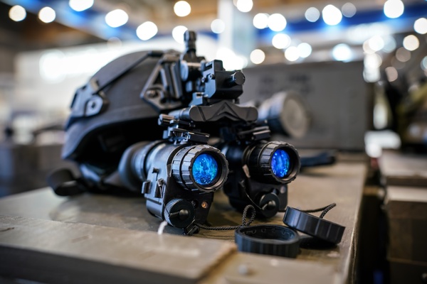 Night vision binoculars are attached to a military helmet. The helmet is lying on a wooden surface in a facility.