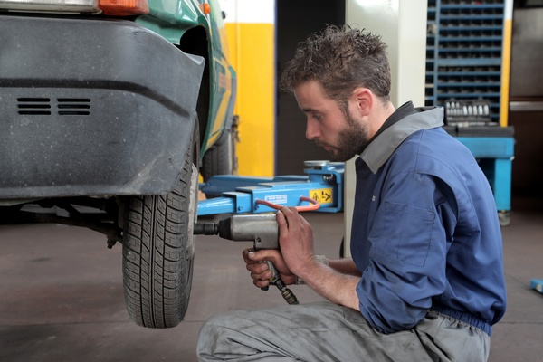 A man works on a car in a garage. He uses a pneumatic wrench as he removes the lug nuts from the wheels.