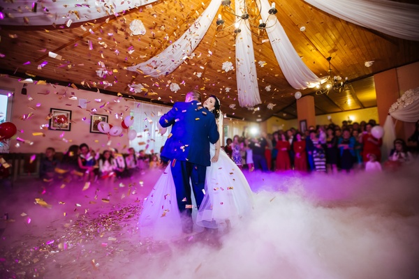 A couple are dancing in the middle of a large room. There is confetti falling from the ceiling onto the couple.