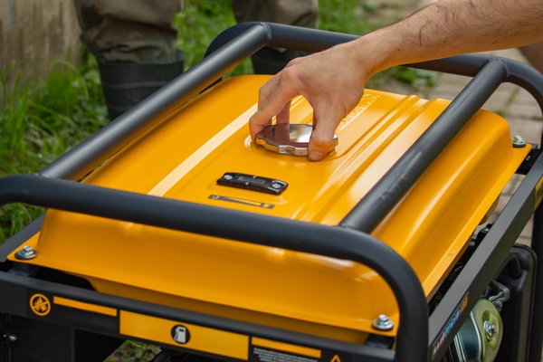 A close-up of the top of a portable backup generator with a man's hand reaching to remove the stainless steel lid.