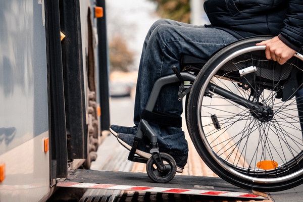 A person in a wheelchair getting on public transportation. They are moving up a small ramp to get on the bus.