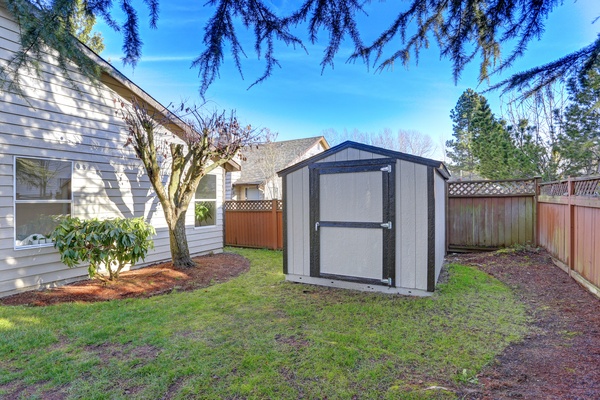 A metal shed constructed in the backyard of a house. It is built on a concrete slab in the middle of the lawn.