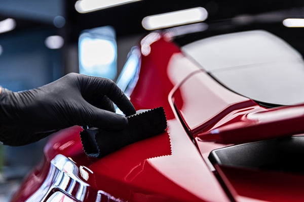 A red sports car surface being wiped with a black cloth by a gloved hand, highlighting a glossy ceramic-coated finish.