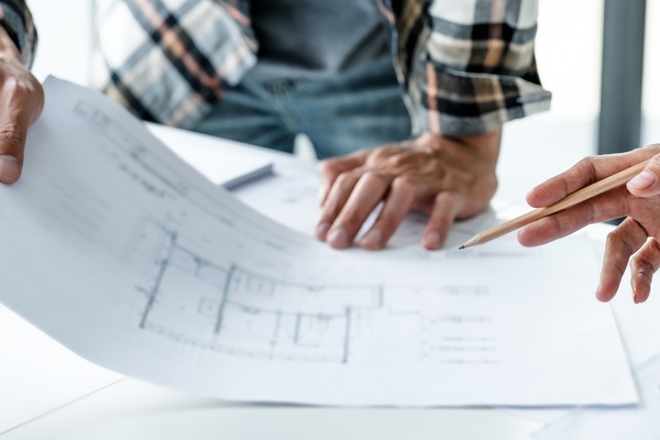A close-up of the hands of two men handling and gesturing at a stack of prints and documents for home construction.