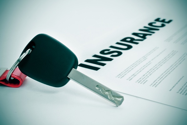 A black car key with a red and silver keychain resting next to insurance paperwork on a white surface.