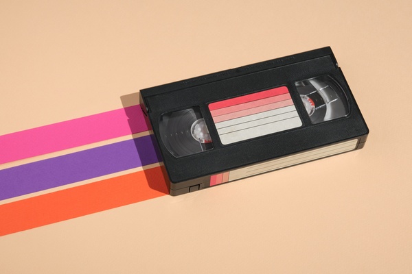 A VHS tape with a gradient on the label laying flat against a beige background with pink, purple, and orange stripes.