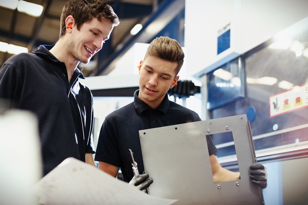 A pair of young workers examining parts against a design on paper and engineering a manufacturing solution.