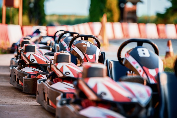 A line of red, white, and black go-karts parked beside red barriers and orange cones on an outdoor track.