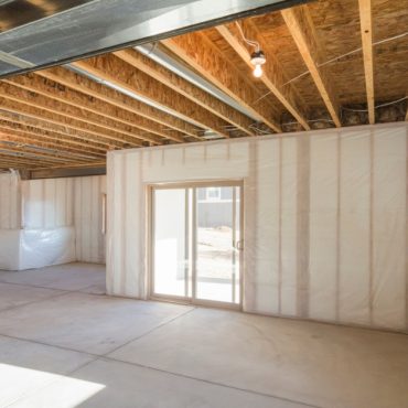 A home's unfinished basement with concrete floors, walls without drywall, a window, and a sliding door leading outside.