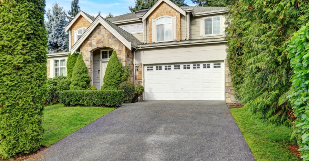 Large two-story house features a stone entry, attached two-car garage, wide driveway, and neatly trimmed greenery.
