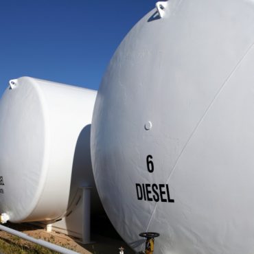 Multiple white industrial tanks line up in a row, filled with diesel and marked with numerical identifications.