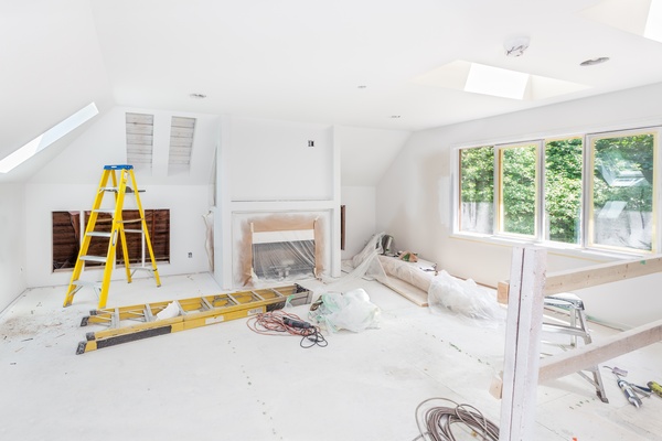 A living room undergoing a remodel with a fireplace covered in plastic, multiple ladders, tools, and bright lights.